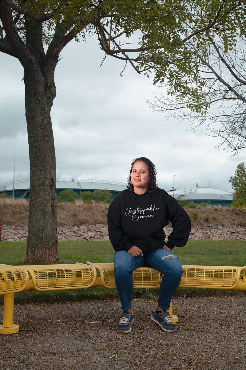 Monica Huertas sits on a bench beneath a tree.